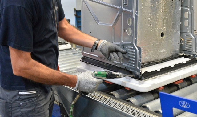 L’ingresso del sito produttivo di Cassinetta oggi nelle mani di Arcelik e, al centro, i dipendenti che lavorano alle linee degli elettrodomestici da incasso (foto Blitz)